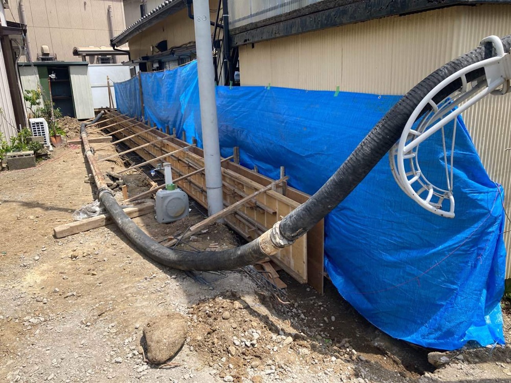 狭い路地でポンプ車を使い、ホースでコンクリートを打設している様子。