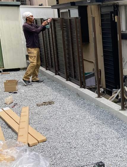 完成したコンクリート壁の上にアルミ製目隠しフェンスを設置中。お隣との視線を遮る工事です。