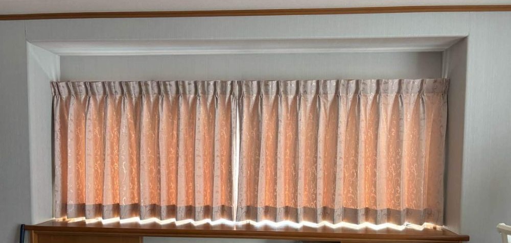 横長窓に明るい色のカーテンを取り付け、部屋が華やかになった様子