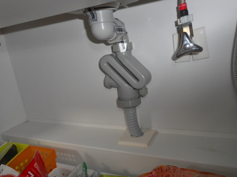 キッチンシンク下で配管の水漏れを確認する様子