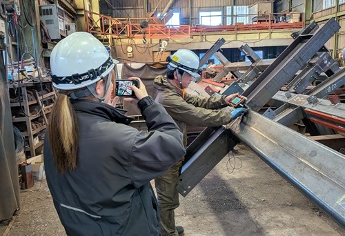 施工管理スタッフが鉄骨工場で、溶接部の検査状況を確認しながら作業を見守っている様子